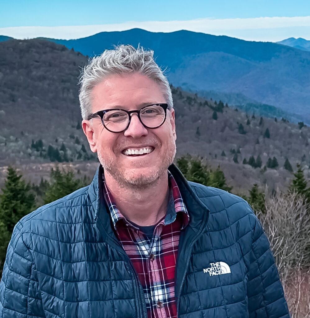 Jay Delaney smiling in front of a mountain landscape